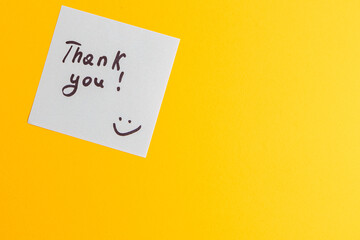 The word thank you on a white piece of paper on a yellow background