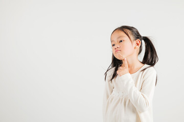 Portrait Asian kid girl deep in thought, standing with chin in hand, pondering a question. Studio...