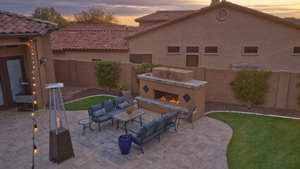 An aerial view of a desert landscaped backyard featuring a travertine pool deck with an outdoor kitchen, fireplace, pool and spa.
