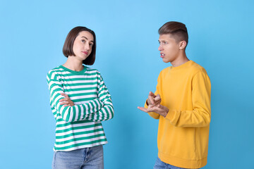 Emotional young couple having quarrel on light blue background