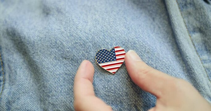 American patriot pinning shiny lapel pin in the shape of a heart with the US American flag. Celebrating patriotism and love of America for 4th of July or to celebrate another patriotic USA holiday.