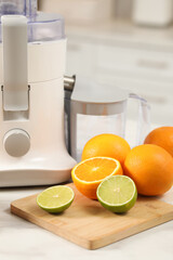 Modern juicer, oranges and limes on white marble table in kitchen, closeup