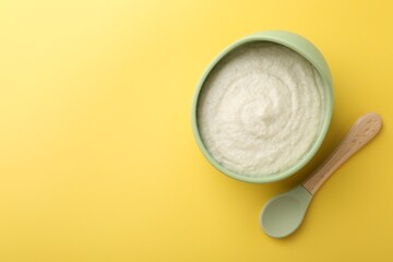 Delicious baby food in bowl and spoon on yellow background, top view. Space for text