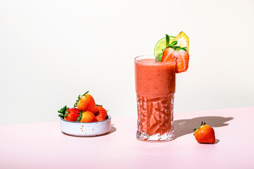 Non-alcoholic mocktail drink with strawberry, banana, syrup, peach juice, lemon and ice in glass. Beige pink background, hard light