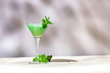 Green alcoholic cocktail drink with liqueur, cream, ice and mint. Beige background, hard ligh