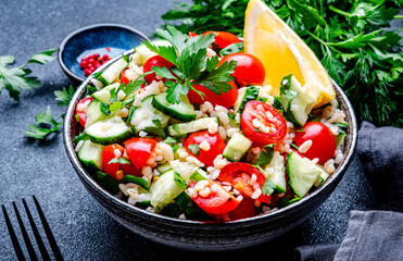 Vegetarian Tabbouleh Middle Eastern salad with bulgur, tomatoes, cucumbers and parsley.. Black background, top view