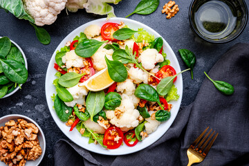 Autumn vegan salad with cauliflower and paprika, tomatoes, spinach with walnuts on gray background, top view