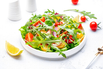 Vegan vegetable salad with tomatoes, cucumber, onion, lettuce and arugula. White background, top view