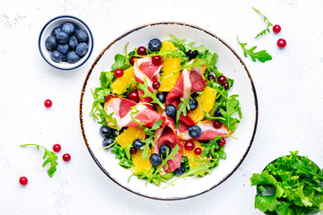 Delicious salad with smoked duck fillet, juicy orange, fresh blueberries, cranberries and arugula on white background, top view