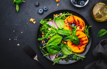 Vegan delicious salad with grilled peaches, fresh blueberries, red onion, walnuts, basil and mixed herbs, black background, top view