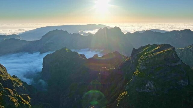 Aerial view at Pico do Arieiro of mountains over clouds with blooming Cytisus shrubs on sunset with sunburst. Madeira island, Portugal. Slide trucking shot