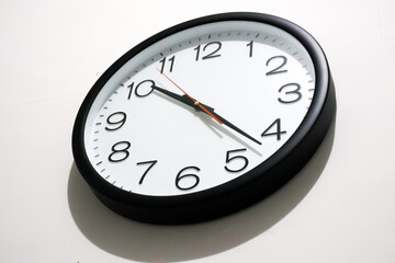 Close-up of a black wall clock with black numerals and white background against a plain white wall. Concepts related to time, time management, schedules, deadlines, simplicity, and punctuality