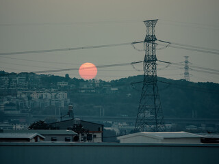 a large orange sun setting over a city with a city in the background.