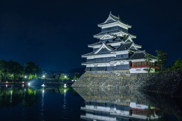 日本　長野県松本市にある国宝、松本城　夜になってライトアップされ内堀の水面に鏡面反射する大天守