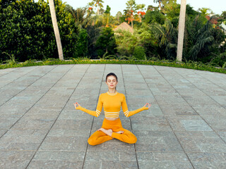 Meditation and mindfulness woman in orange outfit sitting in lotus position on concrete floor