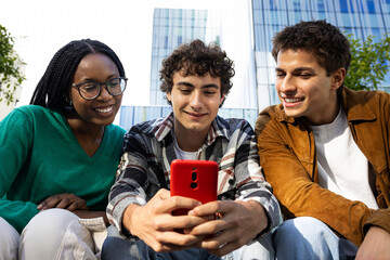 Happy college students looking at mobile phone laughing together. Multiracial teenagers using smartphone outdoors.