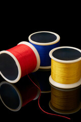 primary colors of spools of cotton embroidery sewing thread isolated black background with reflections, used in detail stitching or decorative fabric and textile industry