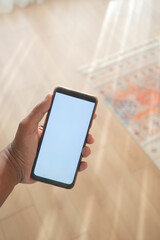A hand is holding a smartphone that has a blank screen in a welllit, bright room