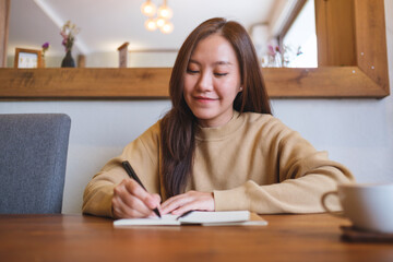 Portrait image of a young woman writing on a notebook on the table