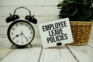 Employee Leave Policies text on paper card with alarm clock on wooden background