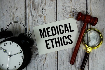 Medical Ethics text on paper card with alarm clock and wooden judge gavel top view on wooden background