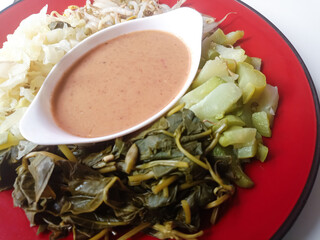 Lotek is a traditional Indonesian food made from various green vegetables and mixed with peanut sauce and has a savory taste on a plate isolated on a white background.