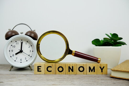 Magnifying glass and alarm clock with wooden blocks alphabet letters ECONOMY text message on wooden background