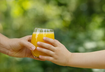 female hand giving glass of orange juice for child with green garden on the background