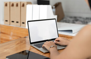 Businesswoman typing on a laptop with a blank screen at a desk in a well-lit co-workspace.