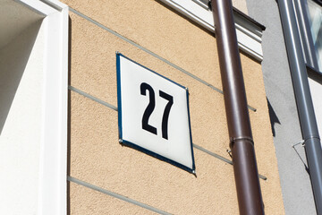Street sign with number 27 on a square metal plate. Detailed view of a building facade with...