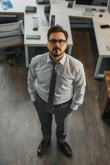 Fototapeta premium A man wearing a white shirt and gray pants stands in front of a desk. He is wearing a tie and glasses