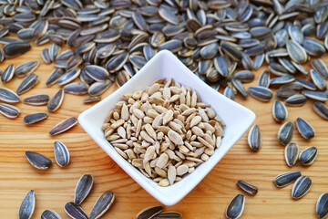 Bowl of roasted sunflower seeds with heap of raw seeds scattered around