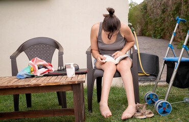 Woman with cerebral palsy sitting in the garden and reading a book, with her walker by her side
