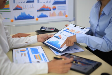 Two businessmen are presenting about statistical data graphs in their company to exchange information.