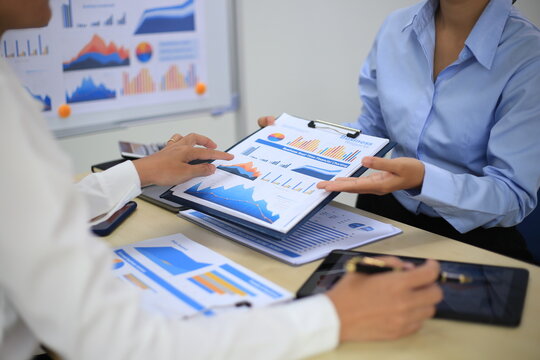 Two businessmen are presenting about statistical data graphs in their company to exchange information.