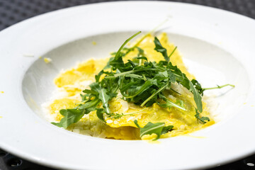 Ravioli, stuffed pasta filled with cheese, arugula topped, grated cheese, served in a lemon zest sauce