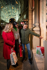 Obraz premium group of friends enjoying holiday shopping and admiring window displays in a cute illuminated street