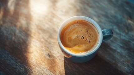 Top view of a cup of coffee on a wooden table, with soft natural light streaming in from the side. No logo, no people.