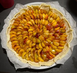 Unbaked Fruit Tart with Sliced Yellow and Red Mirabelle of Lorraine Plums Neatly Arranged on Pastry Dough in a Round Baking Pan, Ready for Baking and Perfect for a Homemade Dessert