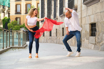 Young dancers having fun in the street while practicing cuban salsa steps with a red veil