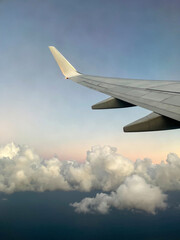 Fototapeta premium The wing of an airplane in flight against a serene sky. Beneath the wing are fluffy white clouds with hints of golden light, at sunset, creating a calm atmosphere.