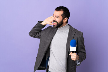 Naklejka premium Adult reporter man with beard holding a microphone over isolated purple background listening to something by putting hand on the ear
