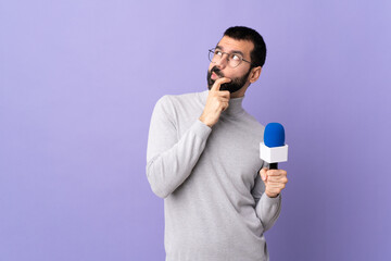 Naklejka premium Adult reporter man with beard holding a microphone over isolated purple background having doubts and with confuse face expression