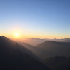 Fototapeta premium Sunrise over mountain ridges with clear sky and foggy valleys