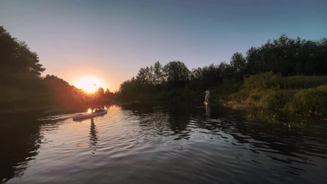 Men floating supboard at sunset river in Summer on beautiful nature. Rowing on stand up paddle board with oar. Outdoors activity on recreation