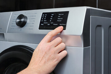 Close-up of hand a adult man press button start automatic washing program switch on the washing...