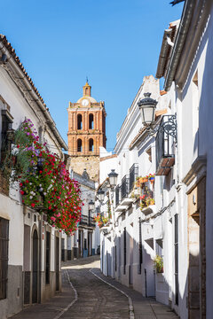 Stone street between white houses with church tower in the background in Zafra with tower of Iglesia de la Candelaria, Badajoz, Spain