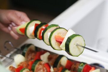 Shashlik cuisine. Metal sticks with vegetable and meat. Raw chicken, onion and bell pepper slices. Grilling food on a picnic. Girl in kitchen. Woman hands preparing dinner.