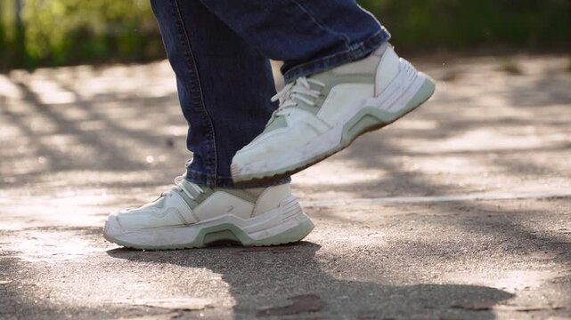 Unrecognizable woman stomps her feet vigorously during workout. Close-up of female feet in sneakers loudly walking in place on asphalt sports ground on sunny day.