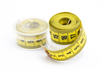 Yellow sewing tape measure rolled up in plastic packaging on a white background. Tailor's tool for accurate measurements. Fabric measuring tape. Sewing accessory for fashion design and dressmaking.